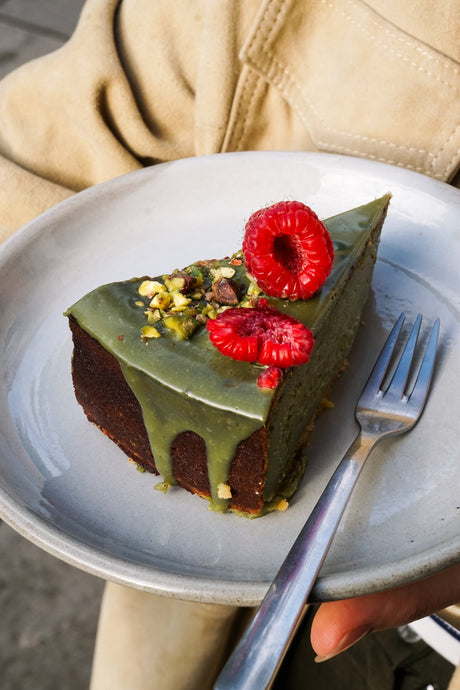 Ein Stück Batida Matcha-Kuchen mit Himbeeren und Pistazien auf einem Teller