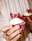 Muffin red velvet z kremem i krwistym cukrowym szkłem trzymany w dłoni