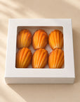 Six Madeleine Pistachio pralines in a white box with a window, top view