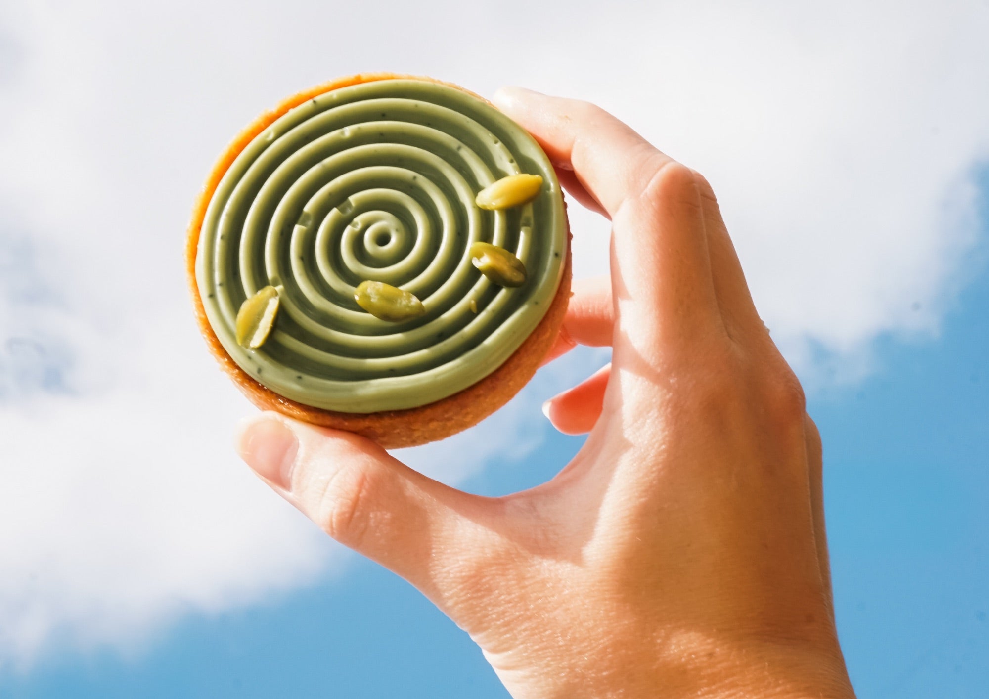Batida Matcha-Tartelette in der Hand vor dem Himmel
