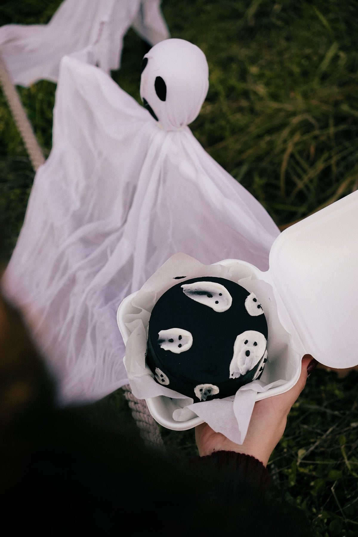 Tort bento z duchami trzymany obok halloweenowej dekoracji