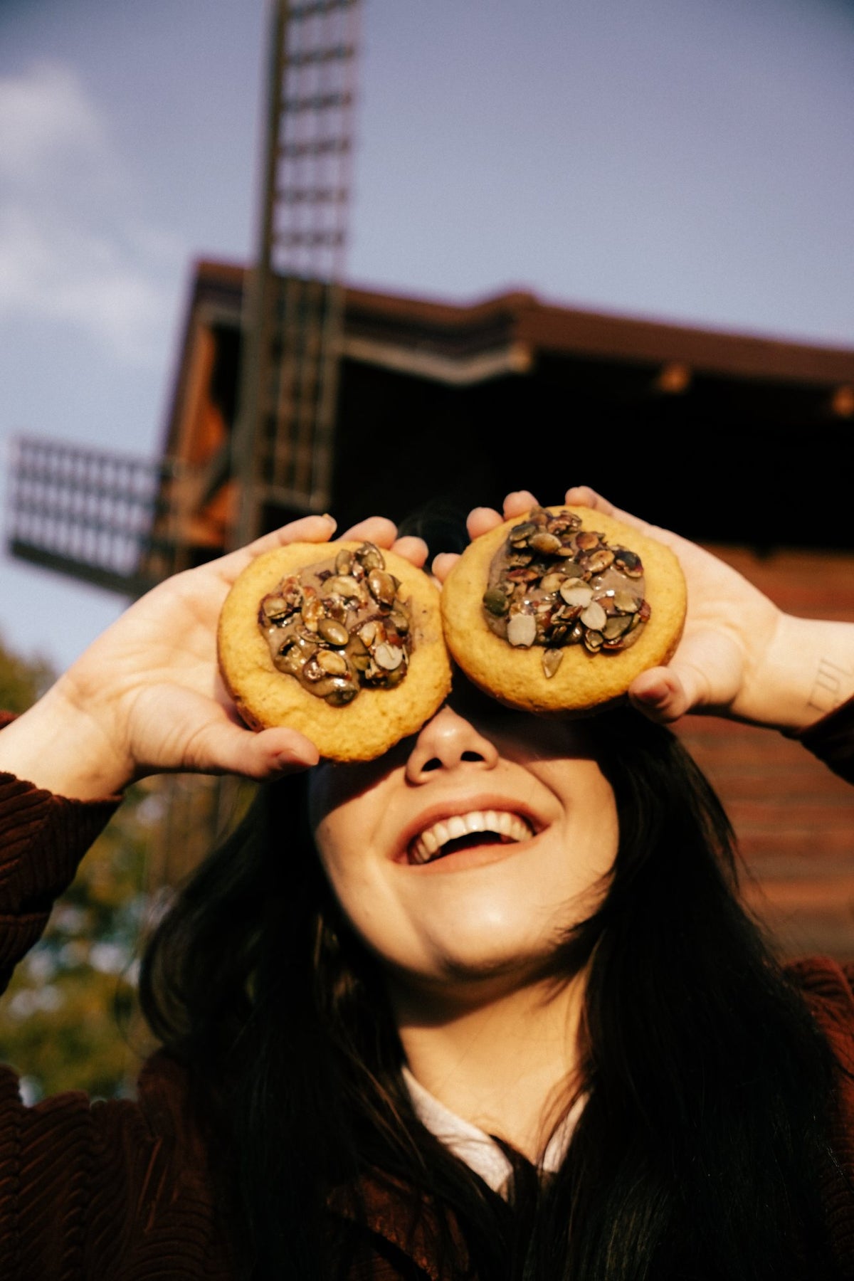 Dwa dyniowe crumble cookies z pestkami dyni trzymane przy oczach