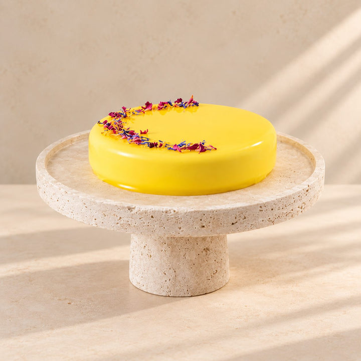 Gelbe Batida-Torte mit Blütenblättern auf einer steinernen Tortenplatte