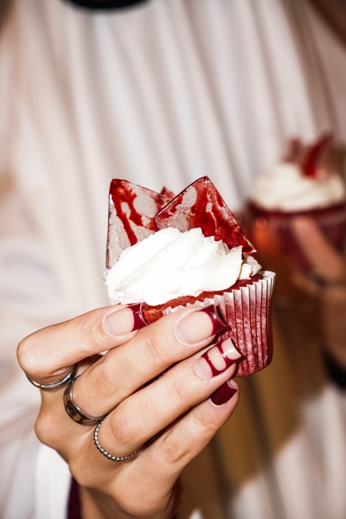 Muffin red velvet z kremem i krwistym cukrowym szkłem trzymany w dłoni