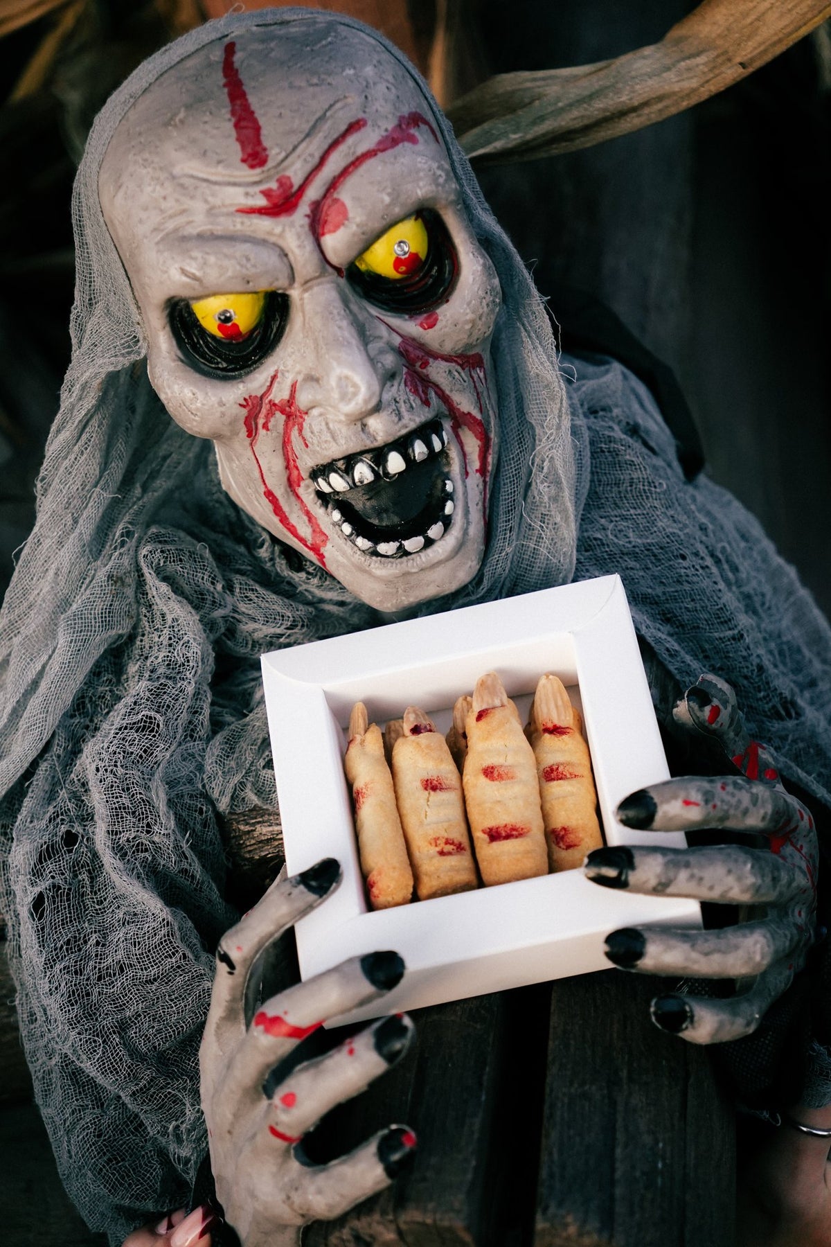 Halloweenowa maska trzyma pudełko ciastek paluchy wiedźmy