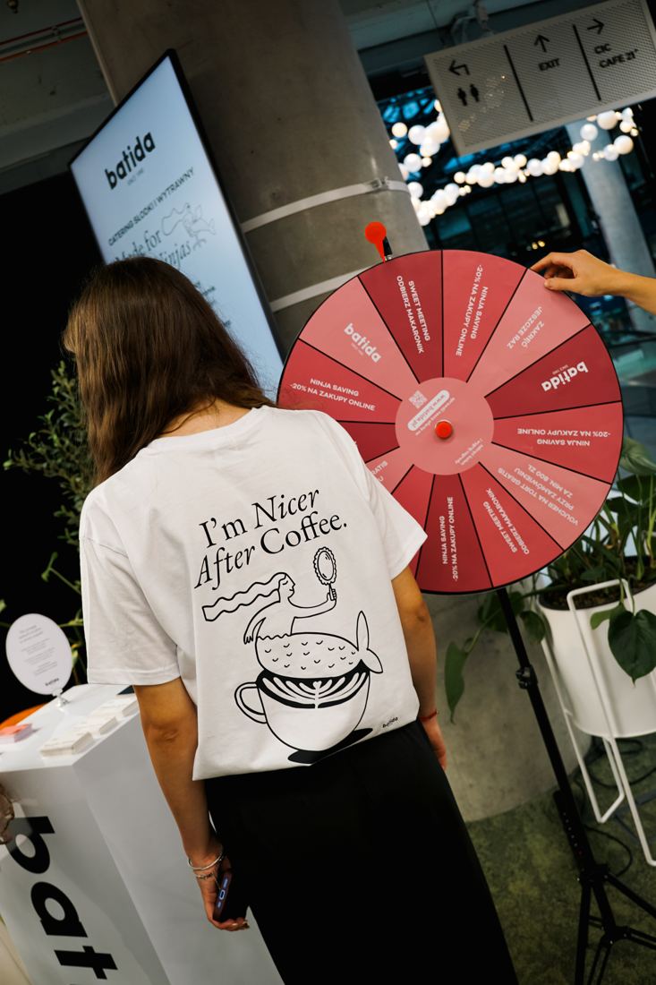 Un membre de l'équipe Batida en t-shirt I'm Nicer After Coffee près de la roue de la fortune lors d'un événement